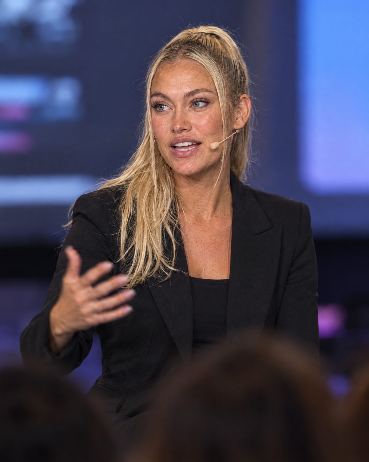 Nina Vellin explaining a point on stage with a headset microphone.